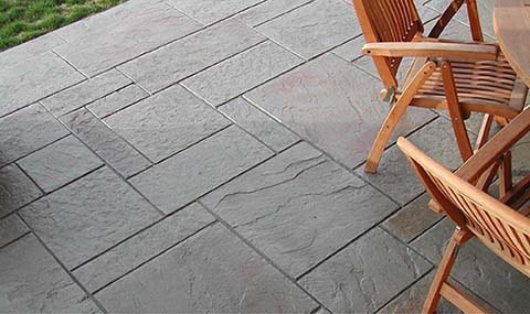 A stamped concrete patio with wooden furniture.
